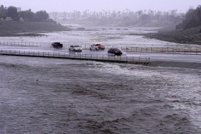 A wide shot is shown of a bridge with vehicles on it, with high waters on either side of the bridge.