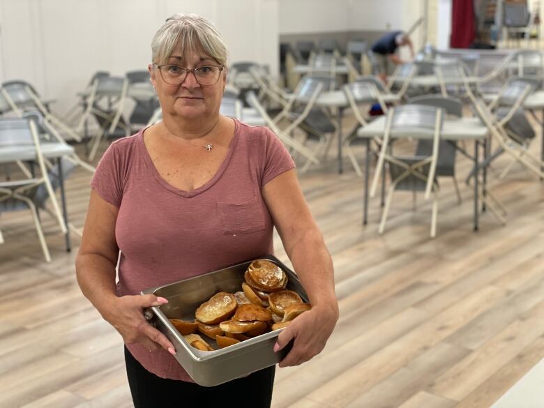 Woman standing in empty hall holding bin of toast