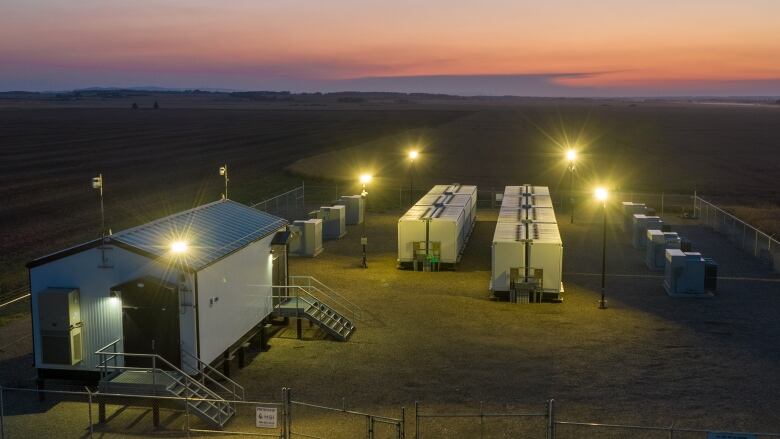 An small industrial facility in a rural field, with a setting sun behind it.