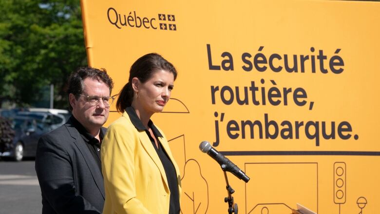 A man and woman stand in front of a road safety sign. 