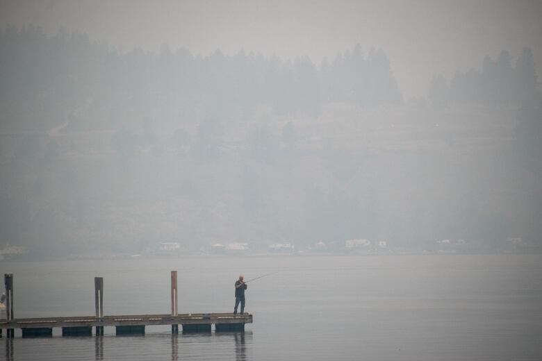 A man fishes on a pier in a lake.