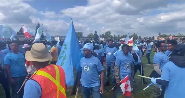 Men in coordinate light blue shirts, some with flags, in a field.