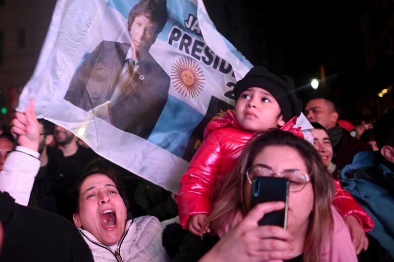 People wave flags and cheer at a political rally.