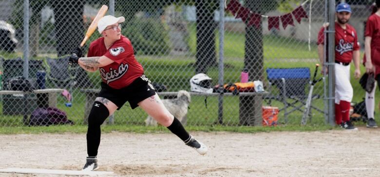 A person in a red jersey and white baseball cap gets ready to swing at a softball at home plate.