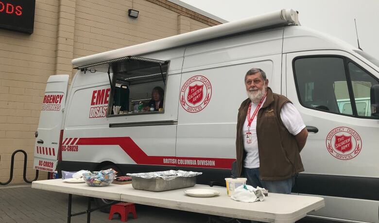 A man stands outside a Salvation Army truck with a table full of supplies.