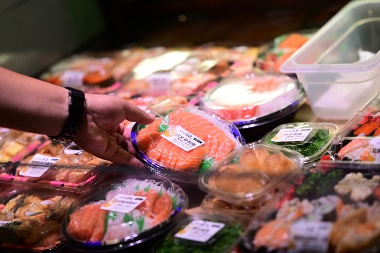 A hand grabs a plastic take-out container with slices of pink fish inside.