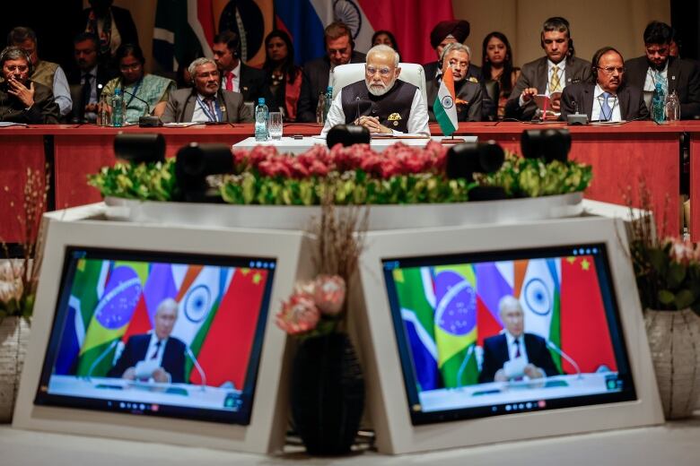 A large conference table is shown with two small video screens displaying a person attending electronically.