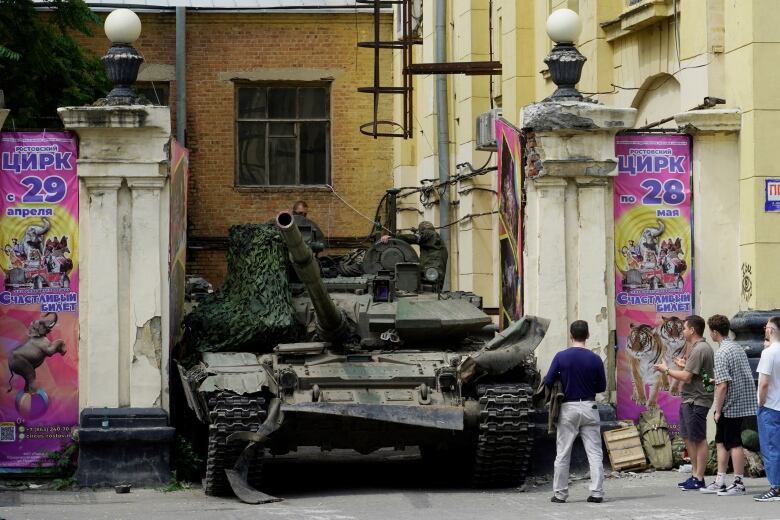 A tank is seen on a city street between two buildings.