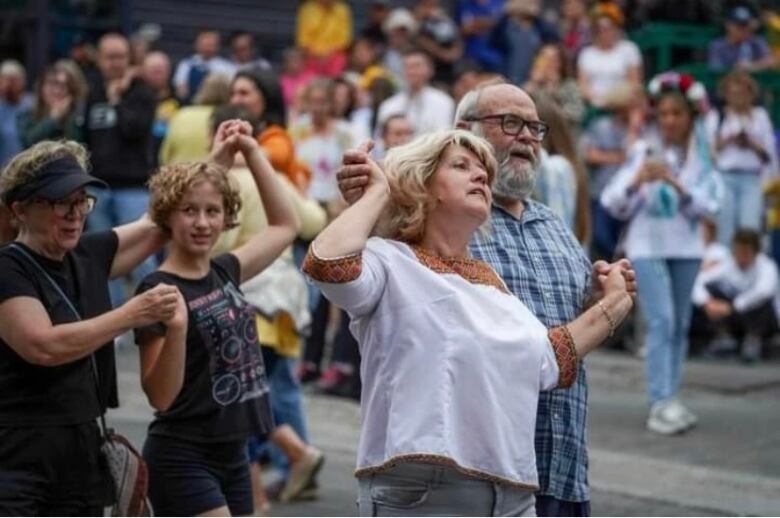 Two groups of two people hold hands and dance in front of a crowd.