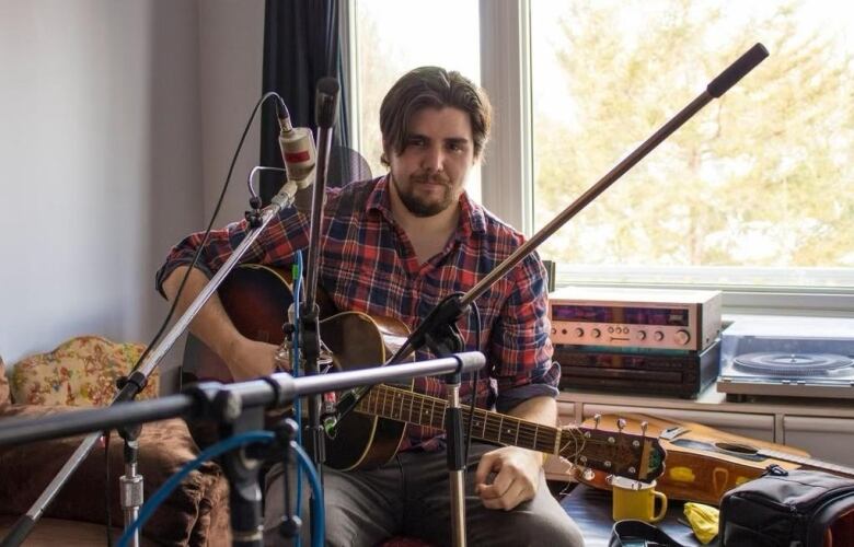 man sits with a guitar in lap and looks at camera. 