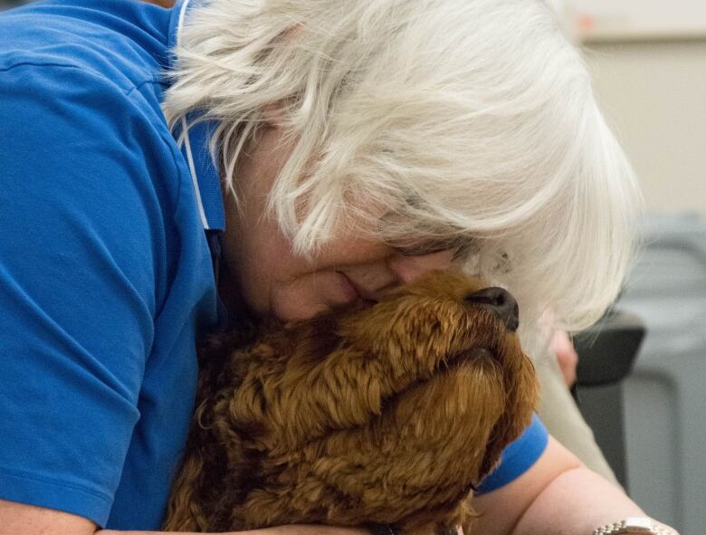 A woman with white hair hugs a curly-haired dog.