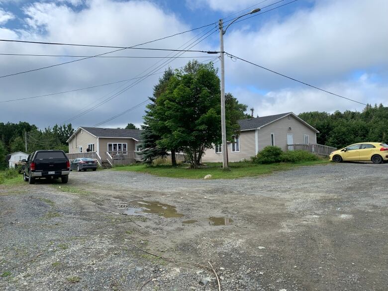 A taupe coloured one storey building with wheelchair ramps sits on a grassy lots with a large gravel parking lot n front of it.