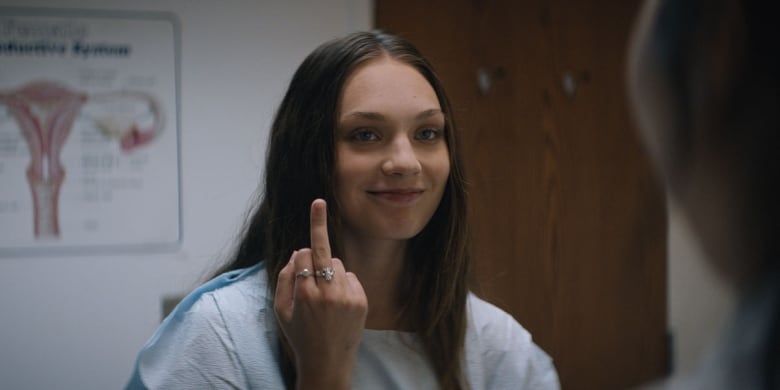 Still frame from the film Fitting In. Maddie Ziegler smiles warmly while flipping someone off.