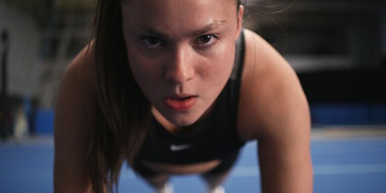 Still frame from the film Backspot. Devery Jacobs does push-ups with a look of focused intensity.