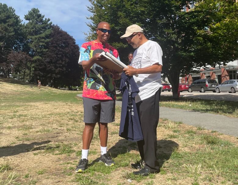 Two men exchange gifts in a grassy park in Vancouver.