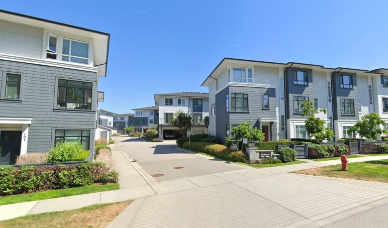 A row of newer-looking white townhouses in a townhouse complex on a sunny day under blue skies.