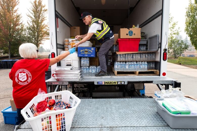 A man wearing a high vis jacket hands a food packet to a woman out the back of a truck.