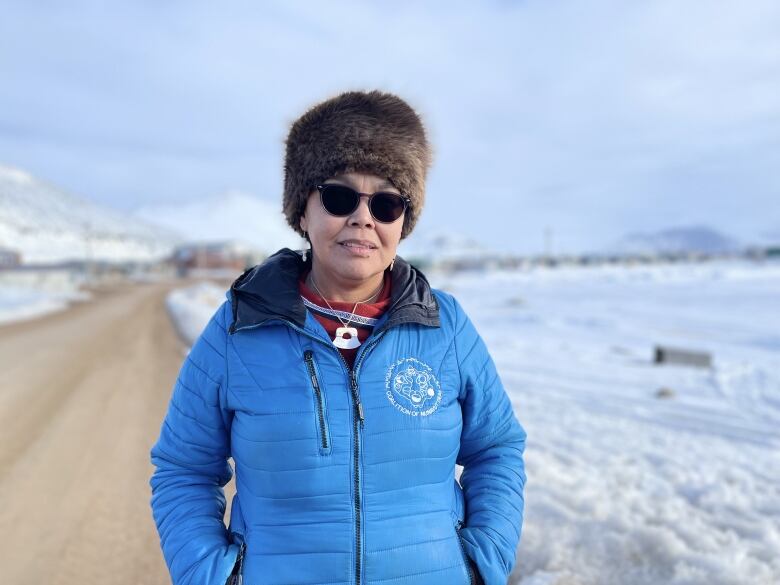 A woman wearing a jacket stands in front of a snowy background.