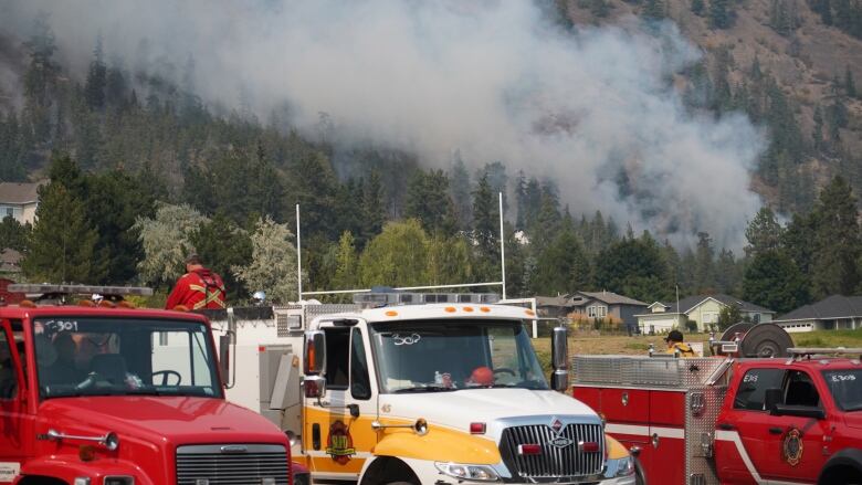 Smoke rises from a hilltop behind a queue of fire trucks.