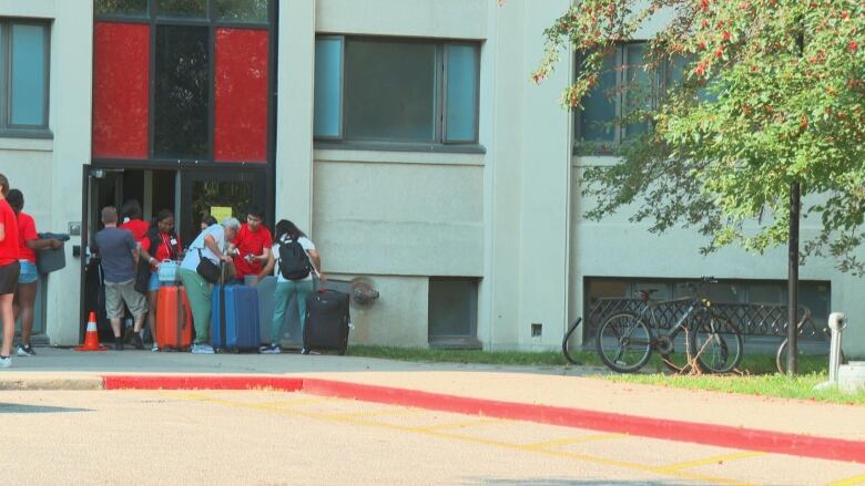 A group of people are pictured taking suitcases into a building.