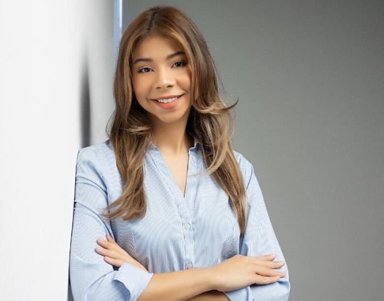 A young lady leaning on a wall with her arms crossed for a photo.