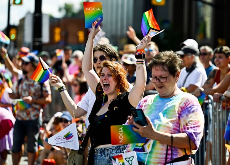 People cheer and wave rainbow flags as they watch a Pride parade.