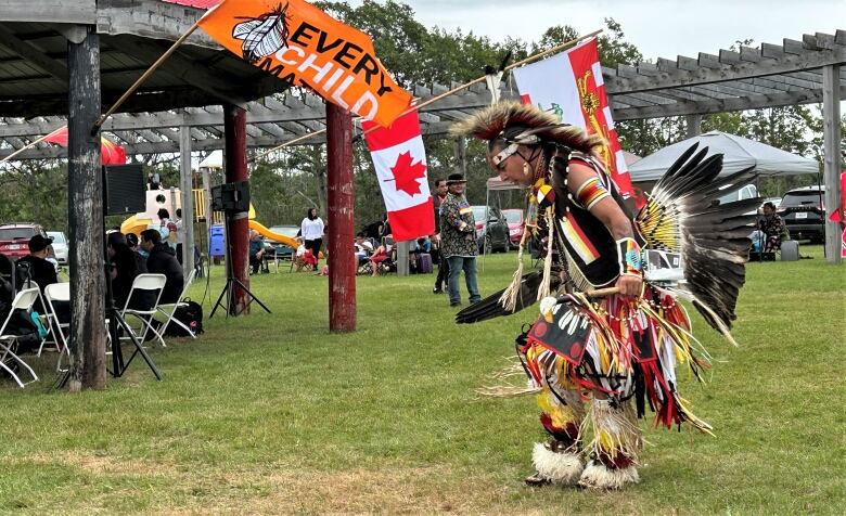 Bert Mitchell dances in full regalia in front of an Every Child Matters flag.