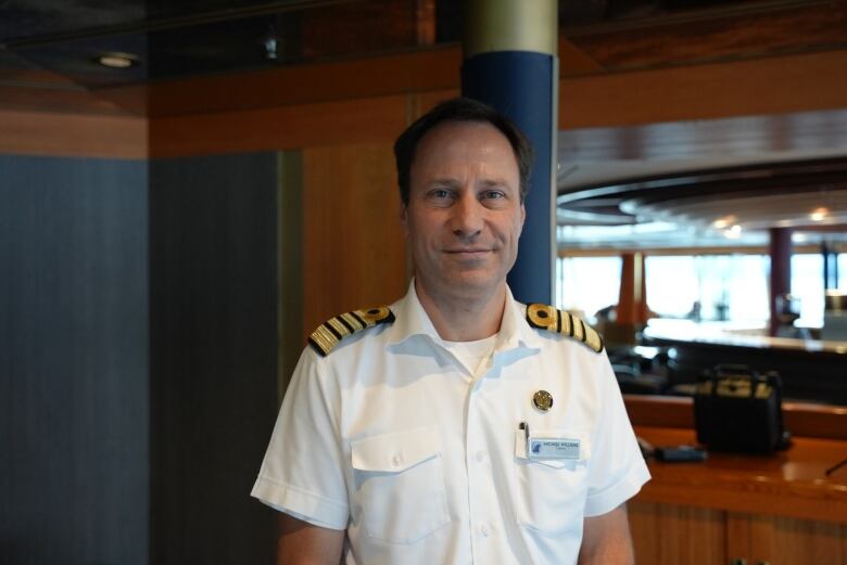 A sea captain stands smiling aboard his ship.