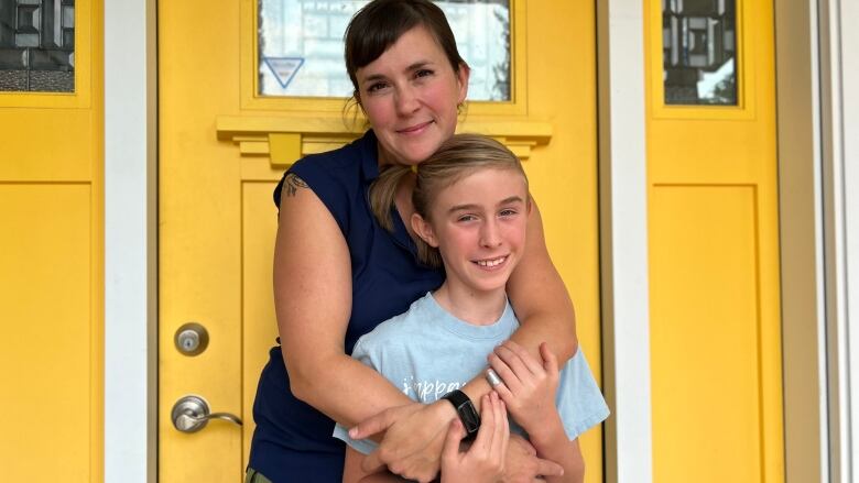 A woman holds her child with a yellow door behind them