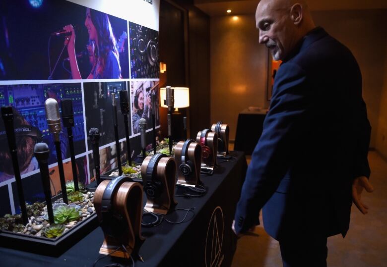 A bald man wearing a dark navy suit looks at several microphones and earphones.