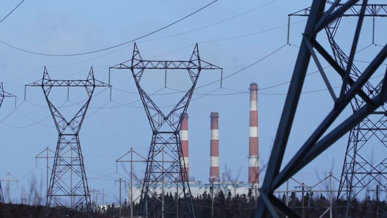 The three smokestacks of the Holyrood Thermal Generating Station behind a line of power lines on a sunny winter day.