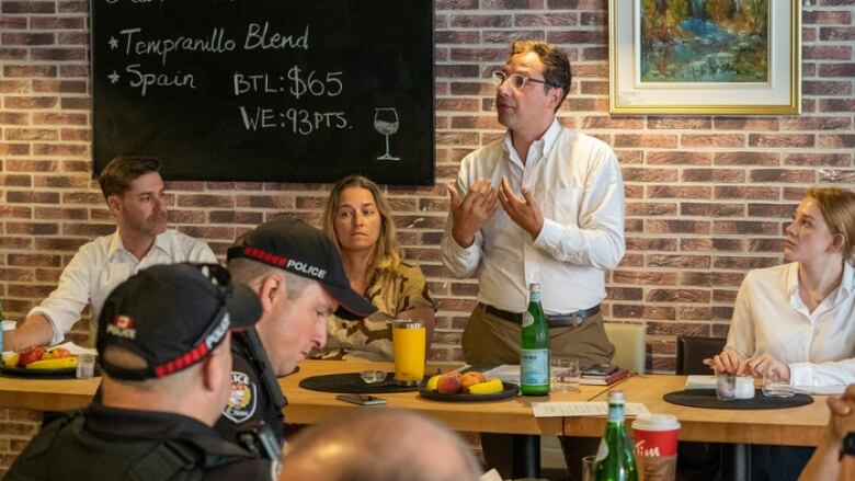 A man stands behind a table as he talks to a crowd.