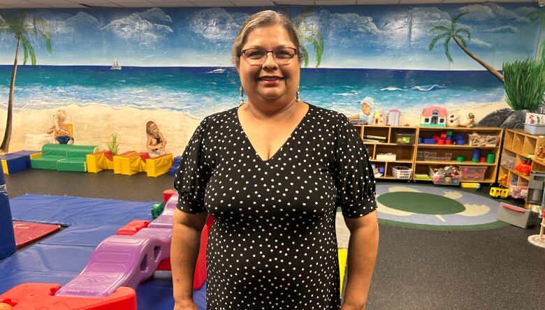 A woman in a black outfit with white dots is pictured in front of gymnasium in a child care centre.