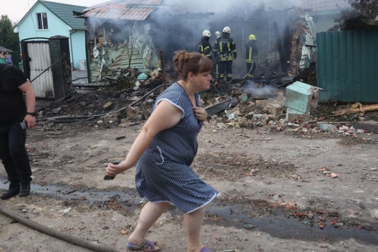 A woman walks past firefighters putting out a blaze at a house damaged in a missile attack outside Kyiv, Ukraine.