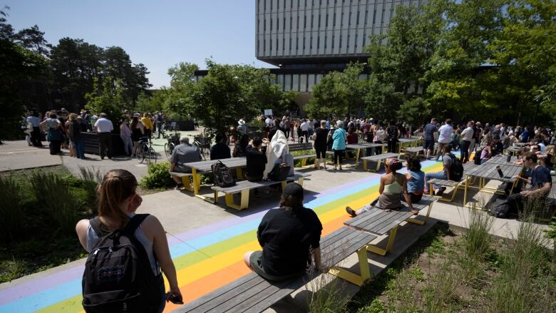 People sit on benches and stand at a vigil