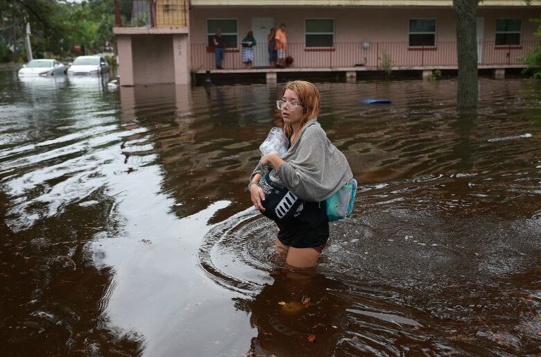 A woman in glasses is shown walking in thigh-high water on a street.