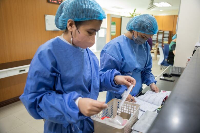 Two nurses in scrubs are seen holding up a piece of paper. 