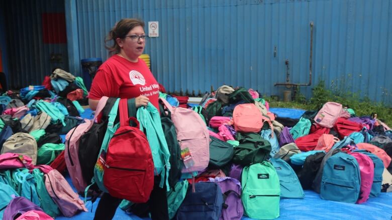 Volunteer in United Way shirt carrying a dozen or so backpacks. 