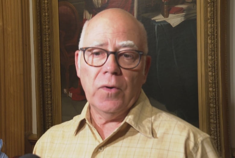 A man speaks while wearing glasses and a yellow shirt.