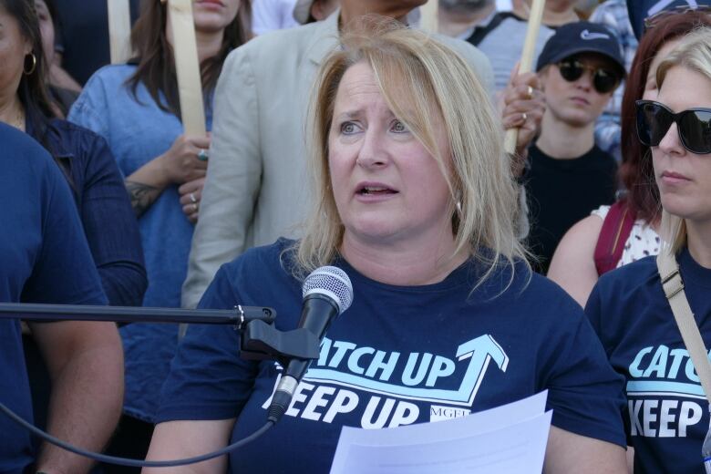 A woman with blonde hair in a navy blue shirt that reads 'Catch up, keep up.'