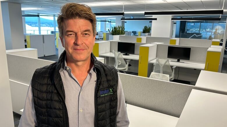 A man wearing a sports vest stands in an office.