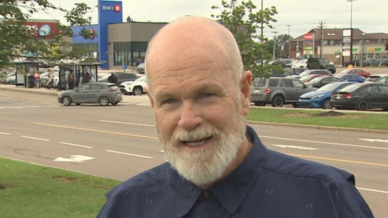 Bald man with beard speaks in a parking lot. 