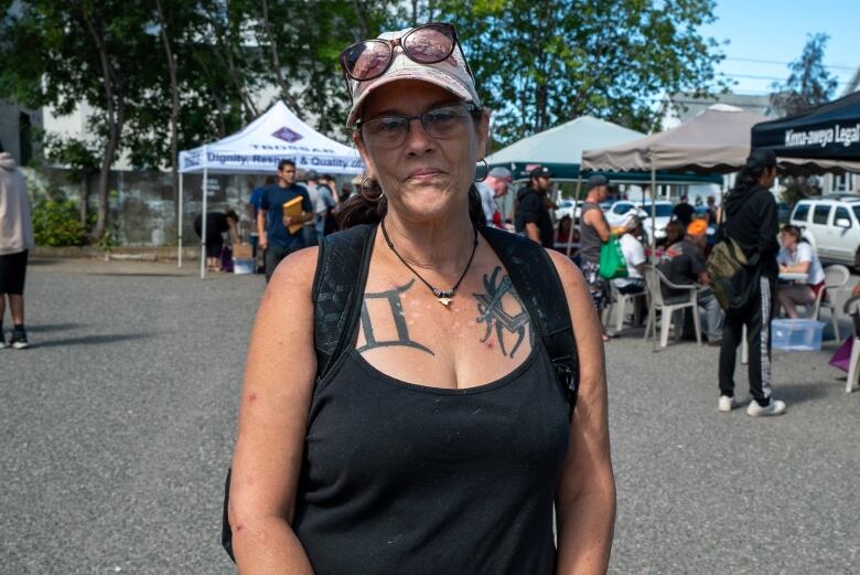 A woman wearing glasses and a baseball cap stands in a parking lot.