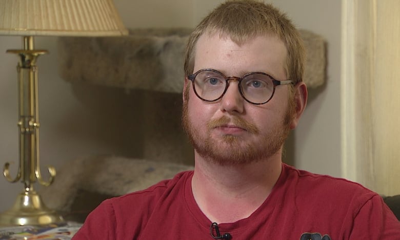 A man in a red t-shirt looks towards the camera.