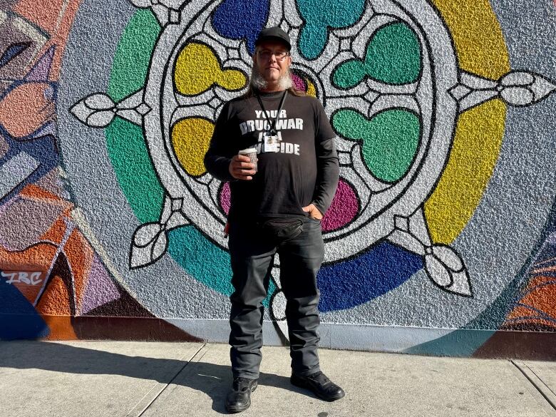 A man holding a coffee and wearing a shirt that says 