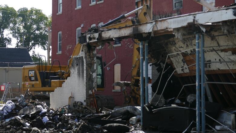 An excavator digs through the rubble of a burned building.