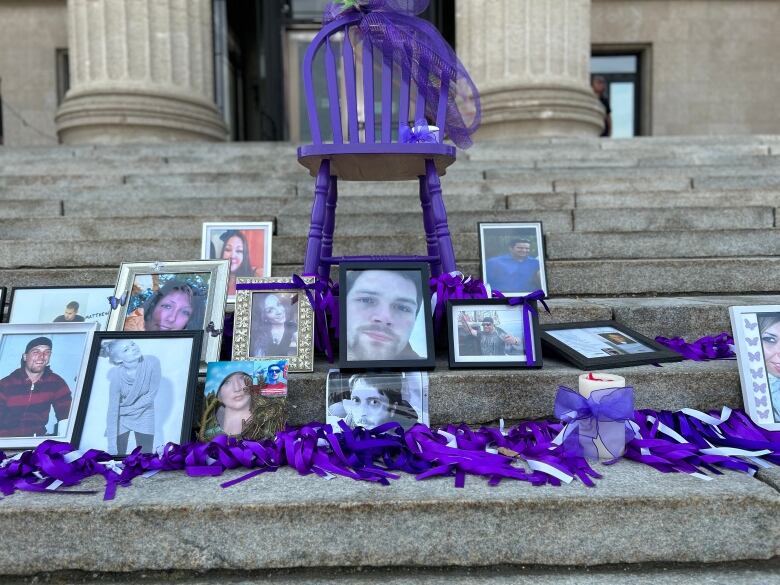 A purple chair balances on the steps of a government legislature next to photos of people who died of overdoses from toxic drug supplies.