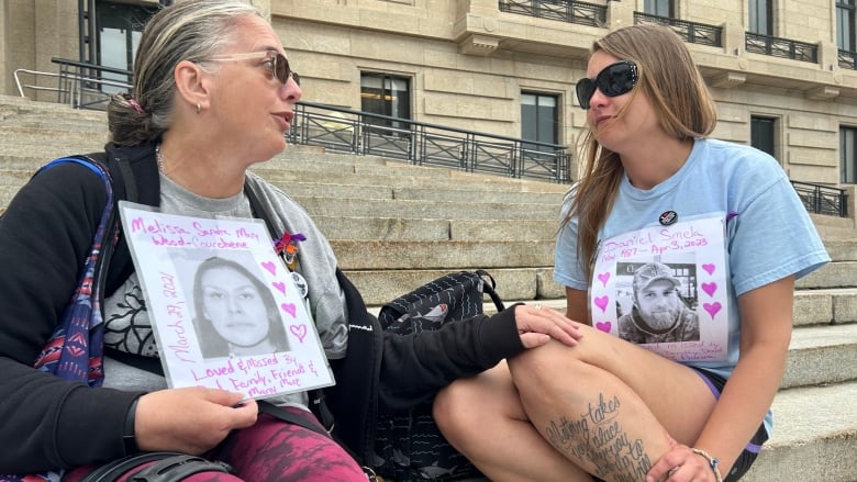 One person puts their hand on another's leg on the steps of a government building during an overdose awareness day event.