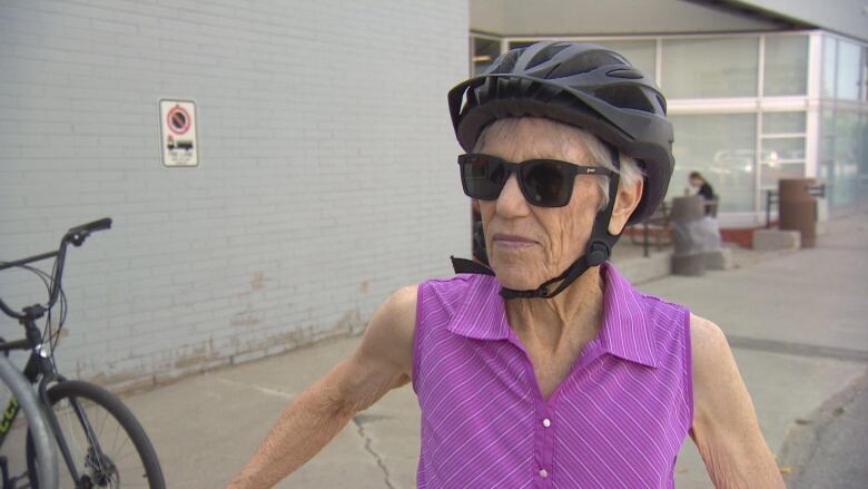 A cyclist in a helmet and purple sleeveless shirt speaks with a reporter outside a mall.