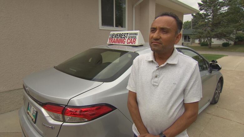 A man in a white shirt stands next to his driving instructor car.